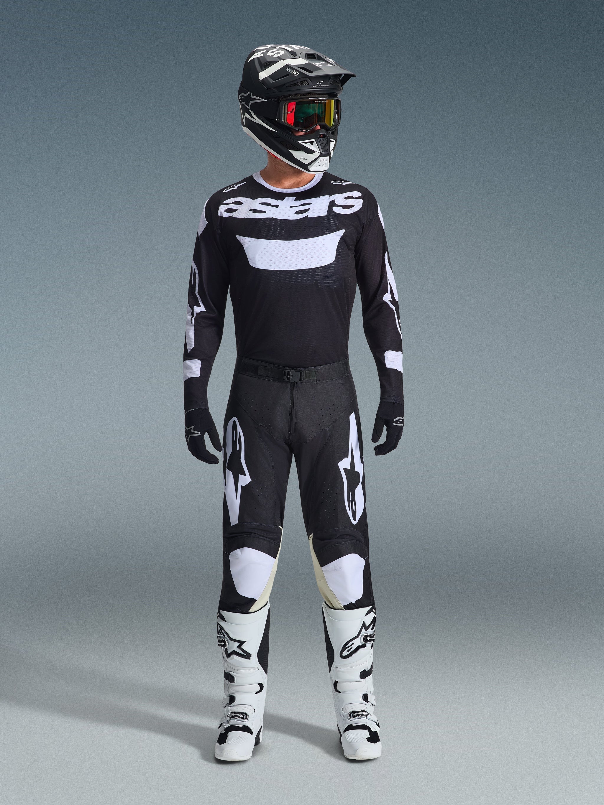 Motocross rider wearing complete racing gear, Alpinestars 2026 Racer Air Riway Jersey in Black and White with 'astars' branding on chest, matching black pants with white accents, white motocross boots, and black and white helmet with goggles, coordinated professional off-road racing outfit