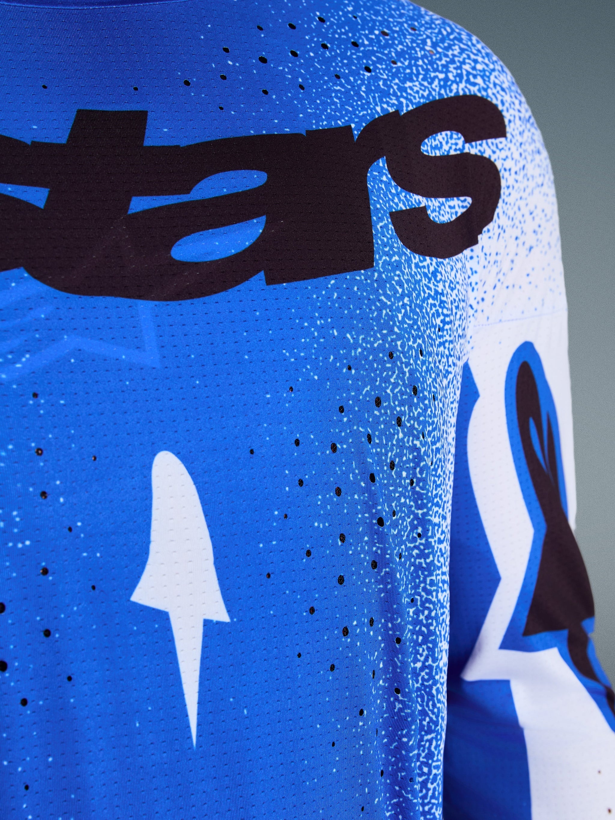Alpinestars 2026 Supertech Scenz Jersey, close-up of Ucla Blue and White design, featuring laser-cut perforations for ventilation, black 'stars' branding, and breathable mesh fabric for professional motocross racing.