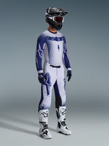 Motocross rider wearing complete professional racing gear, 2026 Supertech Scenz Jersey in light gray and dark blue, matching motocross pants with star graphics, black helmet with red goggles, white and black performance boots, coordinated blue and white gloves for off-road racing