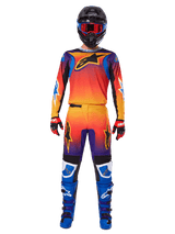 Motocross rider wearing the Alpinestars 2025 Fluid Wurx Gear Set, featuring a vibrant orange, yellow, and blue gradient on the jersey and pants, black Alpinestars logos, paired with blue racing boots, red and black gloves, and a black helmet with red goggles, complete coordinated outfit for off-road racing