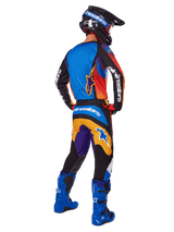 Motocross rider viewed from the back wearing Alpinestars 2025 Fluid Wurx Gear Set, multicolor jersey with blue orange and purple panels, matching pants with white Alpinestars logo on the seat, bright blue boots and a black helmet, coordinated outfit for off-road racing