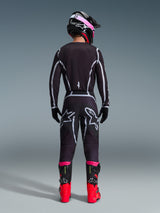 Motocross rider from the back wearing the Alpinestars 2026 Fluid Apex Jersey and matching pants in Black/Gray, featuring white geometric design lines and star logos on the seat, accessorized with a black and pink helmet and red and black racing boots.