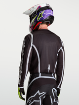 Alpinestars Fluid Apex V2 Jersey, Black and Silver motocross racing top on model viewed from the back, featuring moisture-wicking polyfabric and ergonomic cut.
