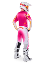 Motocross rider wearing complete racing gear, Pink Fluo and White Limited Edition Supertech AFD MIG Jersey, matching white and pink pants with orange branding, white helmet with pink accents and orange goggles, white and black motocross boots, coordinated outfit for off-road racing