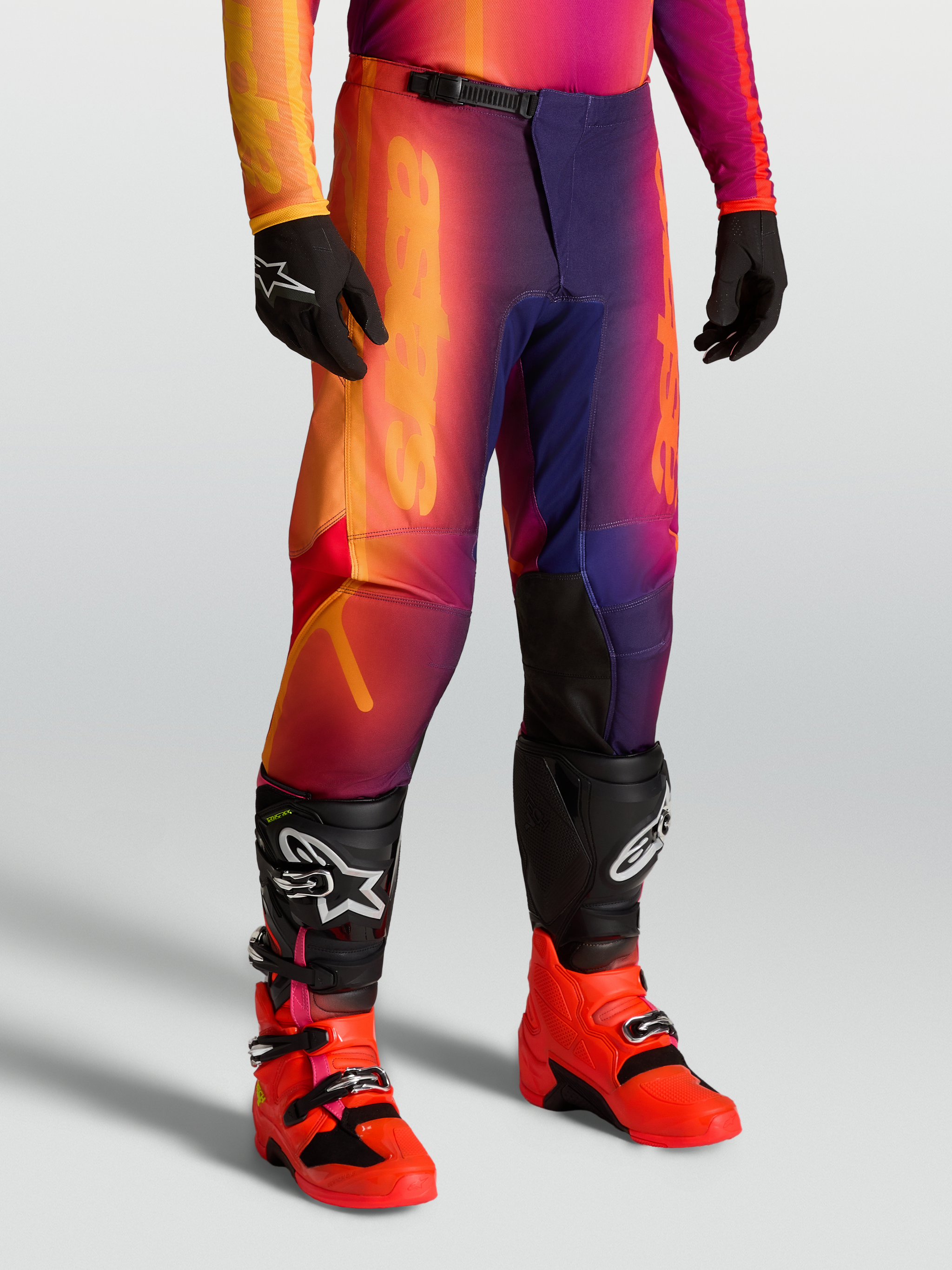 Alpinestars Fluid Kepler Pants for motocross, sport-fit off-road pants in purple and orange, featuring reinforced knees and ergonomic pre-curved design, worn with Tech series boots.