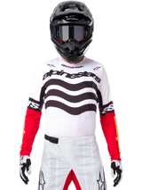 Motocross rider wearing complete racing gear, Limited Edition Techstar Deep Jersey in white and black with red sleeves, featuring wavy graphics and bold Alpinestars branding, white motocross pants, black helmet and goggles, coordinated outfit for off-road racing