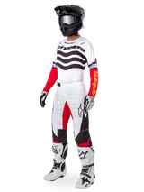 Motocross rider wearing complete racing gear, Limited Edition Techstar Deep Jersey with white and black wavy stripes and red sleeves, matching white and red pants, black helmet, white and black boots, coordinated outfit for off-road racing