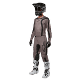 Motocross rider wearing complete racing gear featuring the Alpinestars 2024 Fluid Lurv Jersey in Mud Black, paired with matching pants, black helmet with goggles, white and black boots, and black gloves, coordinated outfit for off-road racing