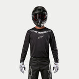 Alpinestars 2024 Fluid Graphite Jersey, Black and Silver motocross jersey, worn by a rider with a black helmet and red goggles, featuring silver Alpinestars branding on the chest, coordinated with black pants and white gloves for off-road performance.