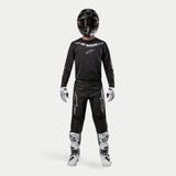 Motocross rider wearing complete racing gear, Alpinestars 2024 Fluid Graphite Jersey in Black Silver, black pants with silver star logos, black helmet with red goggles, white and black boots, white and black gloves, coordinated motocross outfit