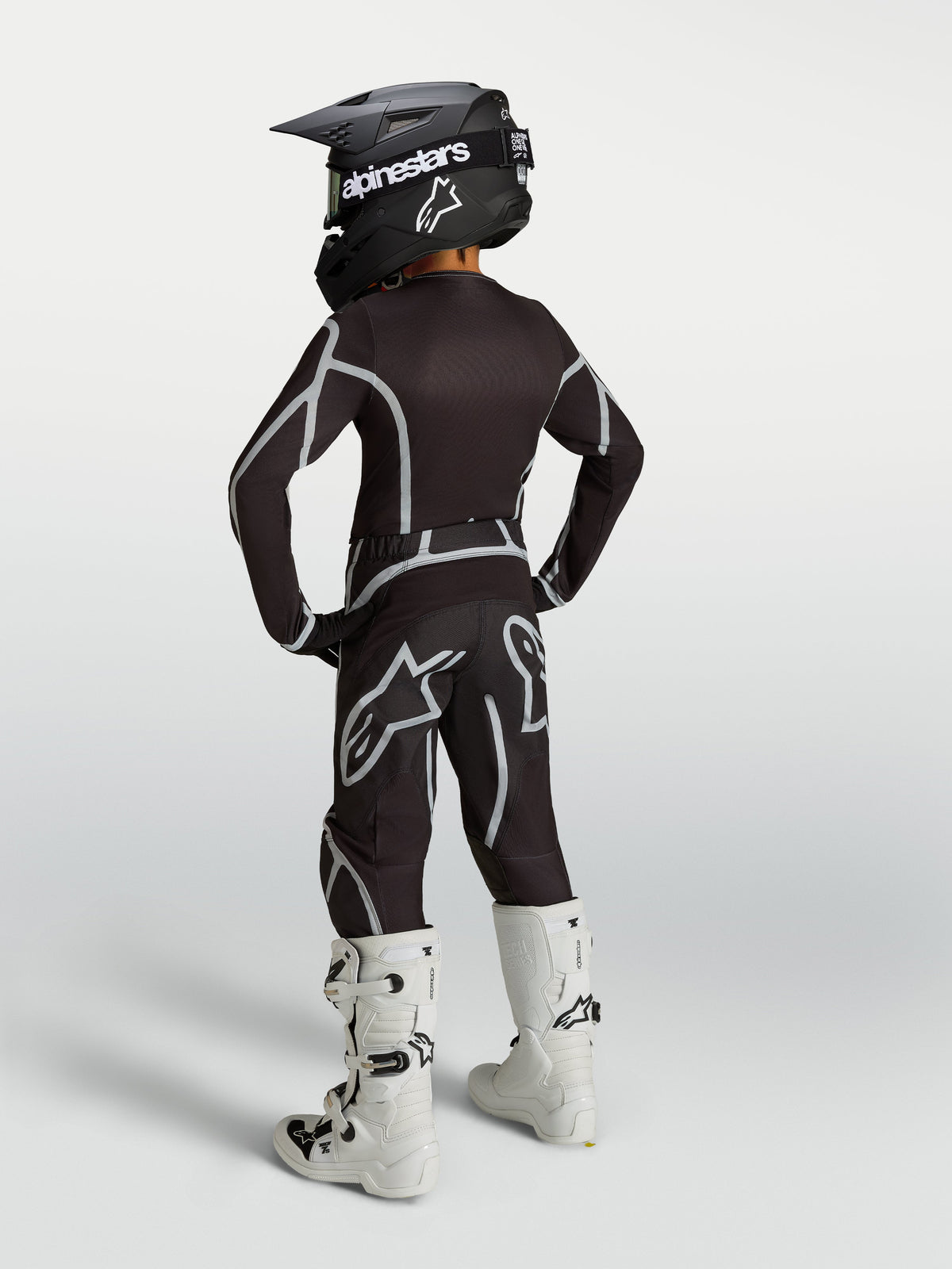 Alpinestars 2027 Youth Fluid Apex V2 black and silver motocross gear set, shown in a rear view with white boots.