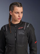 Alpinestars Stella ST-2 Air Jacket, Women's motorcycle jacket in Black, featuring mesh panels for airflow and 'Alpinestars Exploration Equipment' branding with coordinates, red logo accent on the chest, worn by a model with braided hair.
