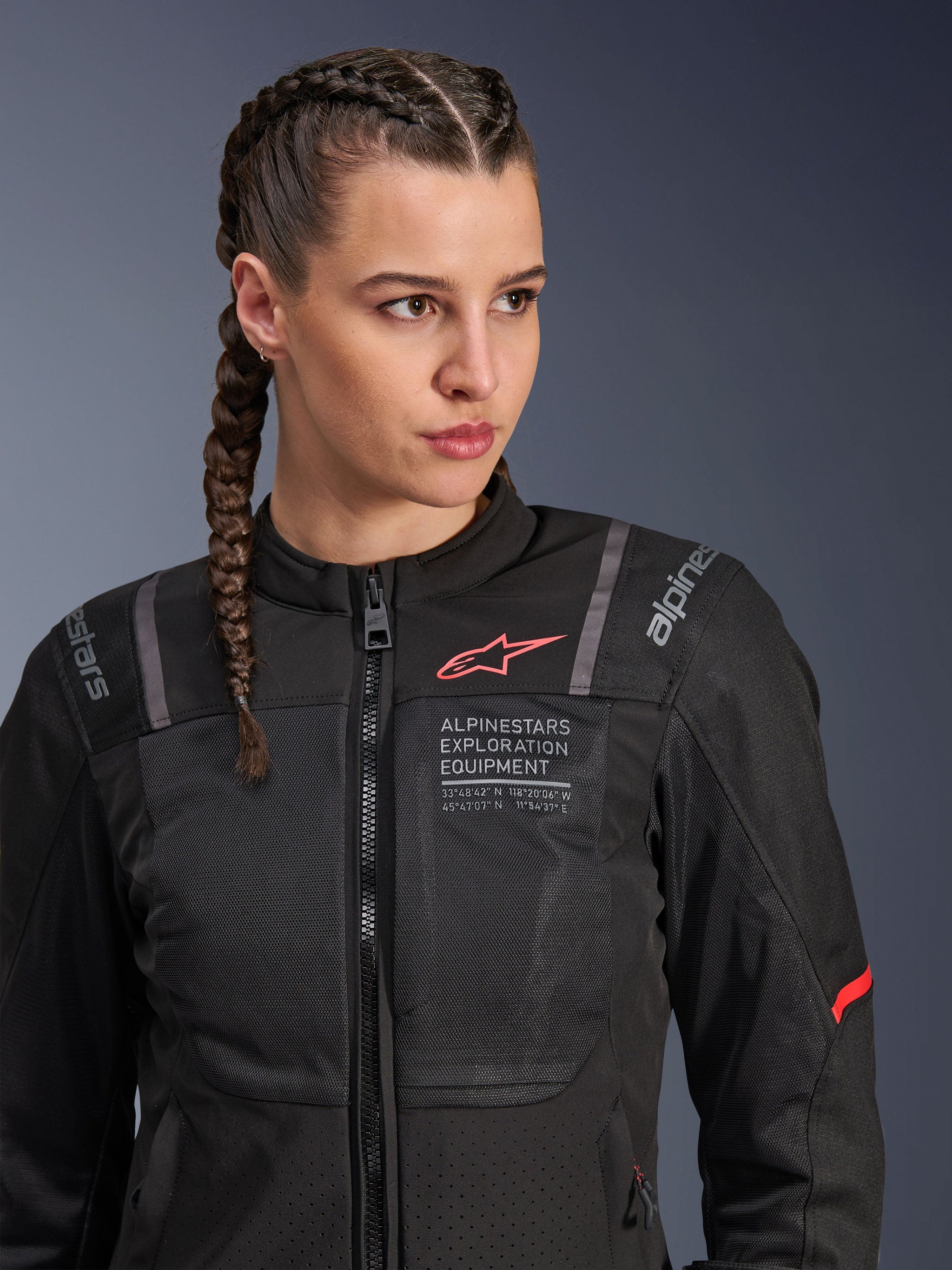 Alpinestars Stella ST-2 Air Jacket, Women's motorcycle jacket in Black, featuring mesh panels for airflow and 'Alpinestars Exploration Equipment' branding with coordinates, red logo accent on the chest, worn by a model with braided hair.