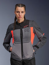 Alpinestars Stella ST-2 Air Jacket, Woman's Motorcycle Jacket, Deep Gray and Fluo Coral, worn by model with braided hair, featuring tech mesh panels for airflow, laser perforations, and 'Alpinestars Exploration Equipment' branding on the chest, summer touring gear