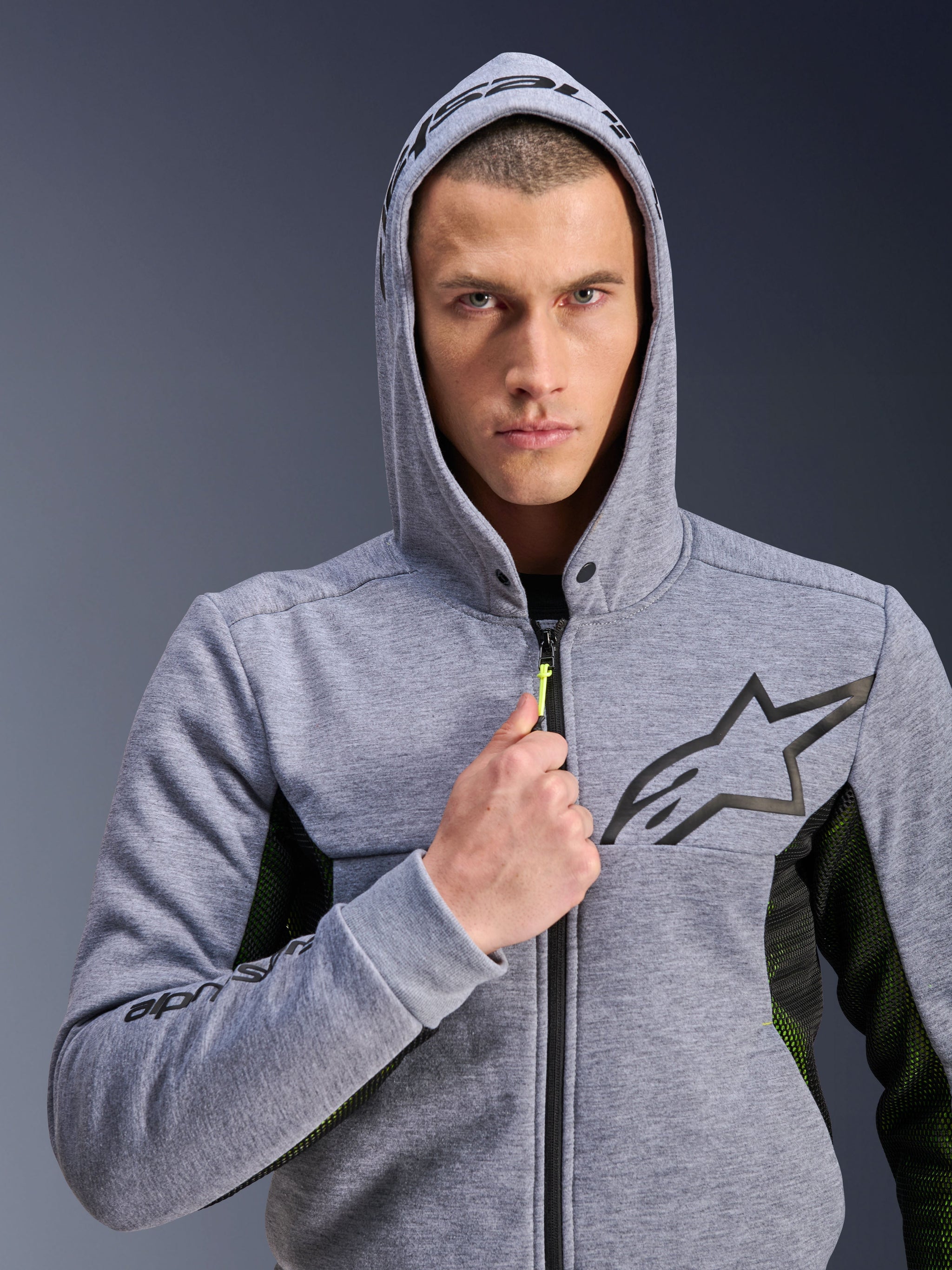 Alpinestars Chrome Air Sport Hoodie, Gray Heather Black, motorcycle hoodie worn by a man with the hood up, featuring a black star logo on the chest, neon yellow zipper pull, and mesh side panels for ventilation, urban riding style