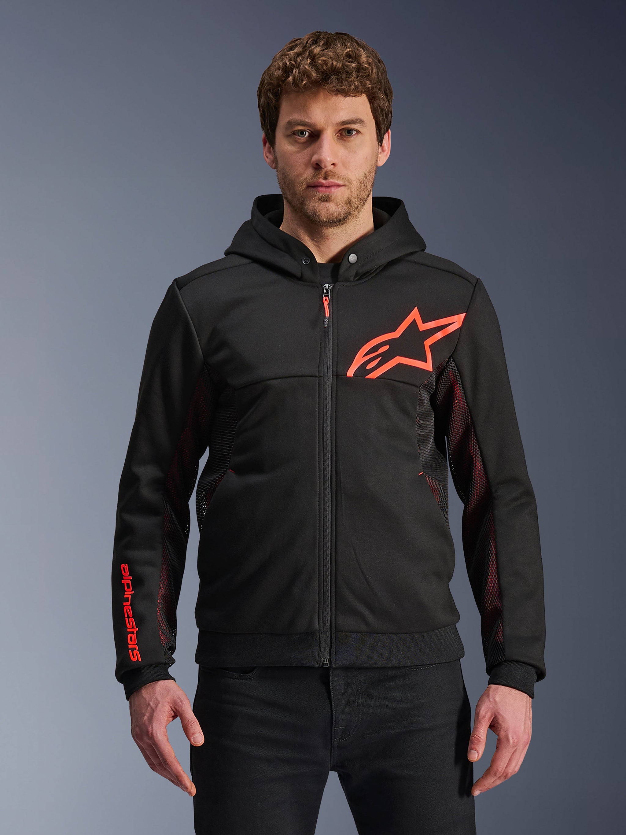 Alpinestars Chrome Air Sport Hoodie, Black zip-up hoodie with red fluo star logo and sleeve accents, red mesh side panels for ventilation, casual urban riding gear worn by a model