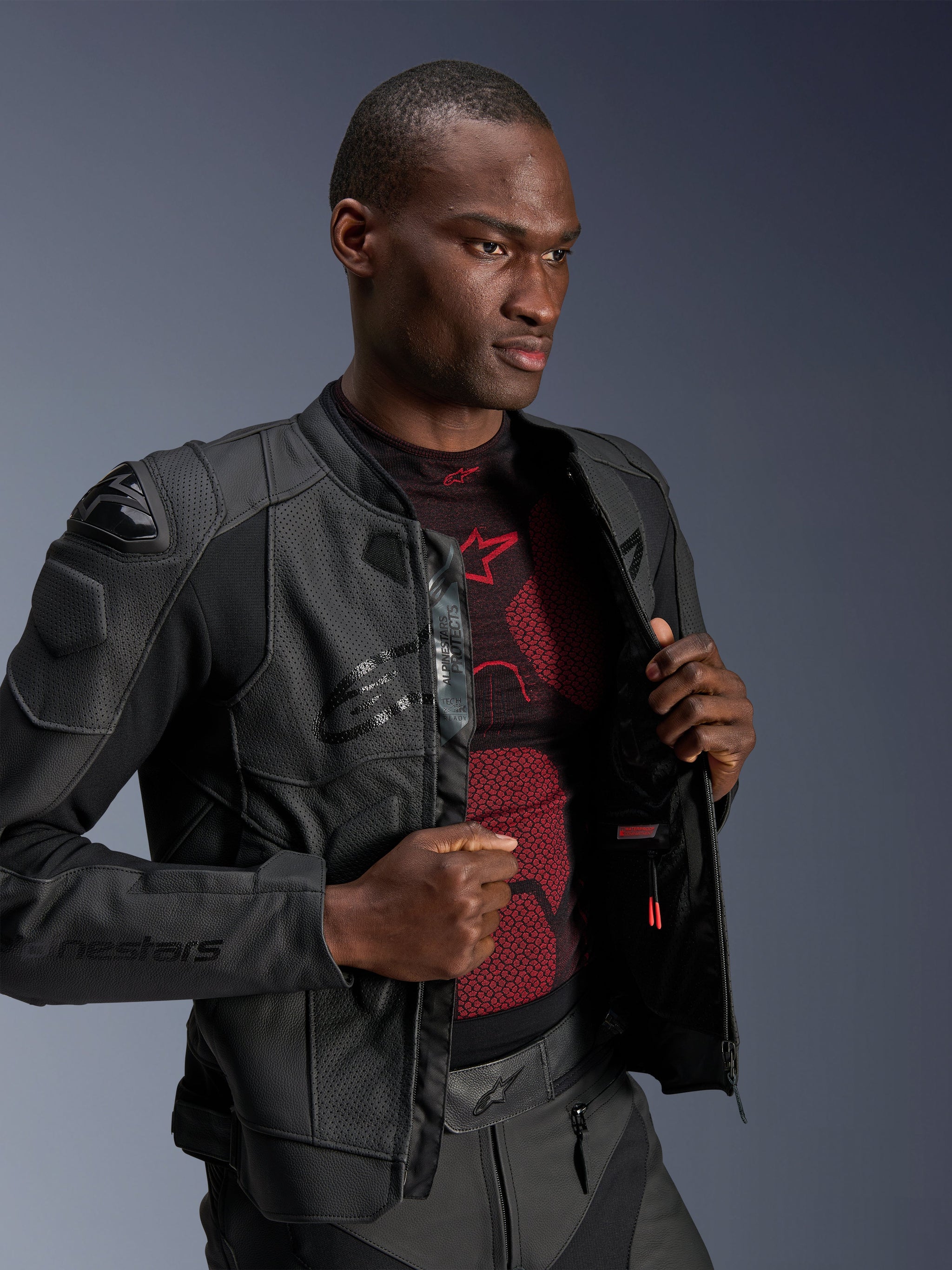 Alpinestars Dusk Airflow Leather Jacket, Black Black, worn by a male model over a red and black base layer, featuring perforated leather panels, external DFS shoulder sliders, and a performance sport fit.