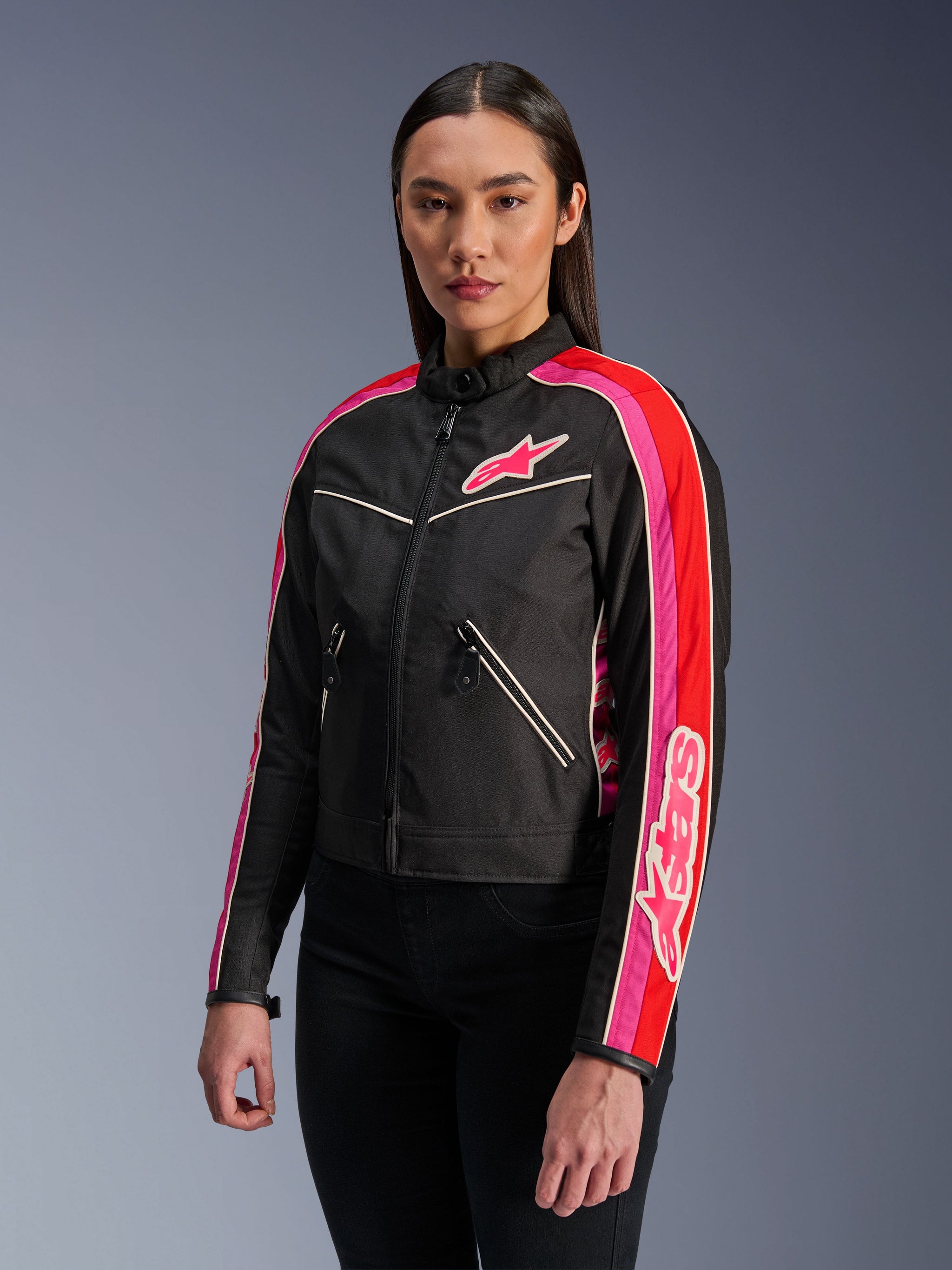 Woman wearing the Alpinestars Stella T-Dyno WR Jacket in Black Bright Red Fuchsia, textile motorcycle jacket with a vintage-inspired biker fit, featuring vibrant fuchsia and red stripes on the sleeves and a chest logo, paired with black pants.