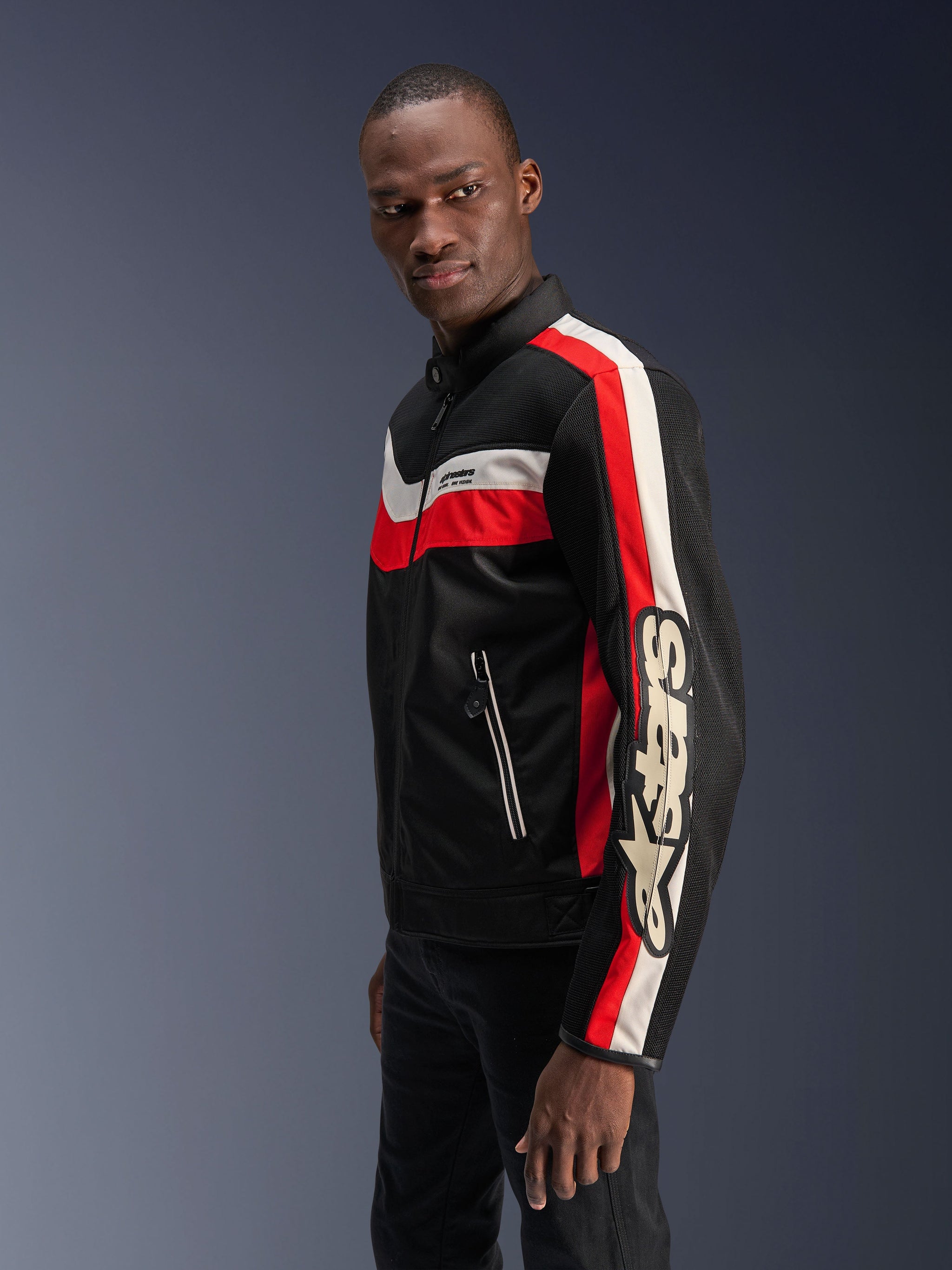 Male model wearing the Alpinestars T-Dyno Air Jacket in Black, Bright Red, and Ecru, vintage-inspired textile motorcycle jacket featuring 3D mesh panels, bold red and off-white stripes, and prominent Alpinestars branding on the sleeve.
