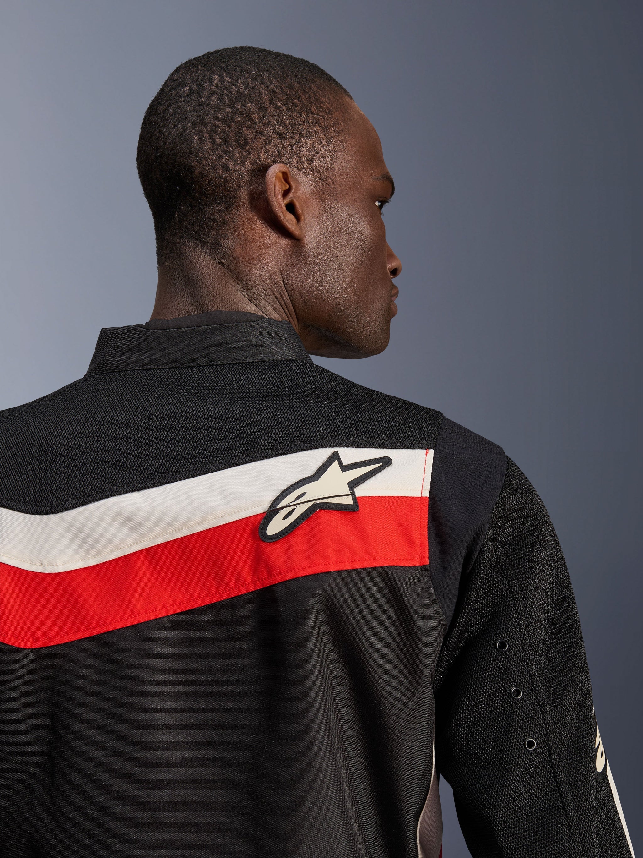Alpinestars T-Dyno Air Jacket, Black Bright Red Ecru, close-up view of upper back and shoulder, featuring horizontal red and ecru stripes with a white Astars logo, breathable 3D mesh panels on the yoke and sleeves, modern classic textile motorcycle jacket