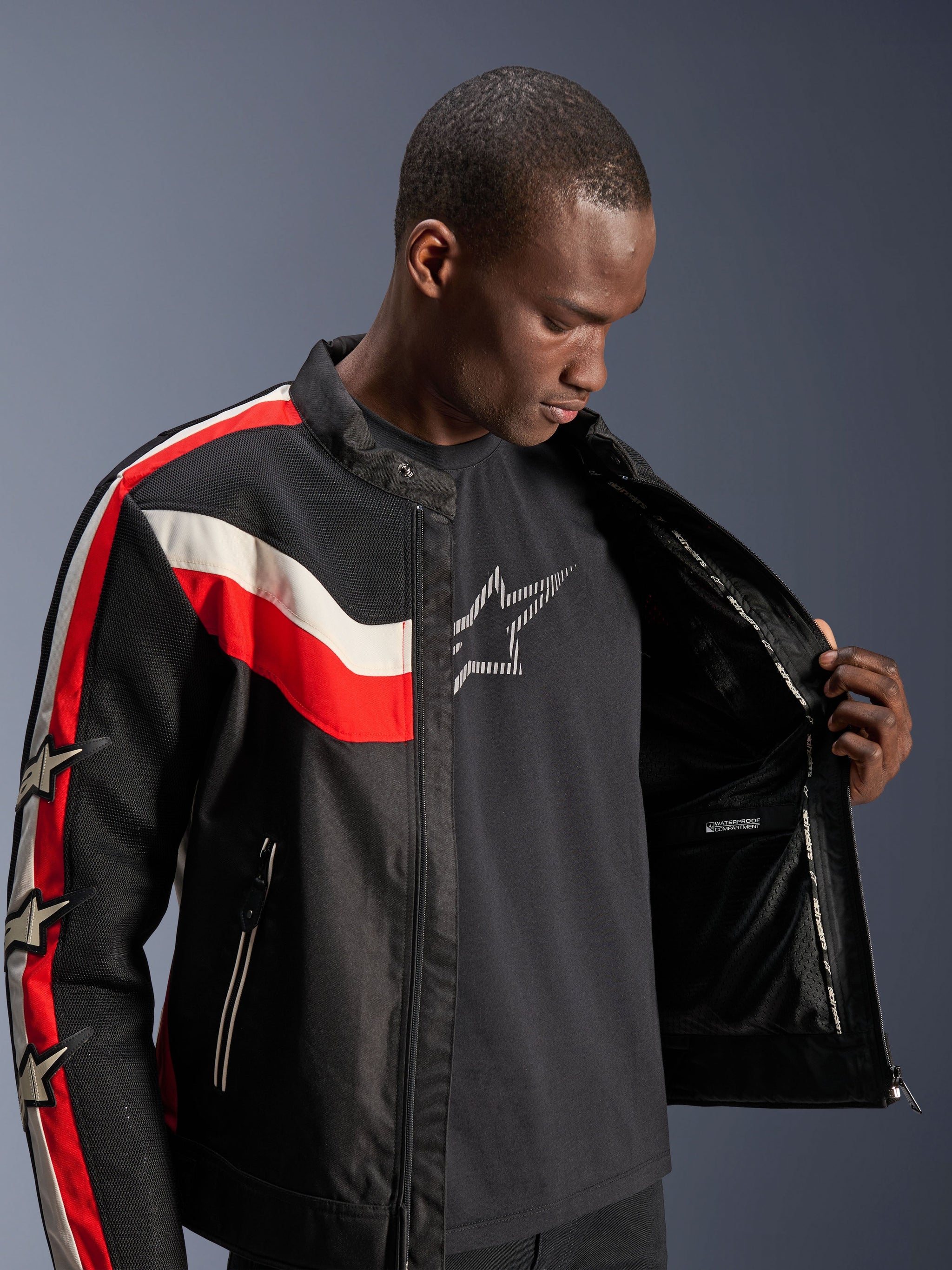Alpinestars T-Dyno Air Jacket, Black Bright Red and Ecru, male model opening the jacket to show internal lining and waterproof compartment, vintage-inspired textile jacket with 3D mesh panels and star logos, modern motorcycle riding gear