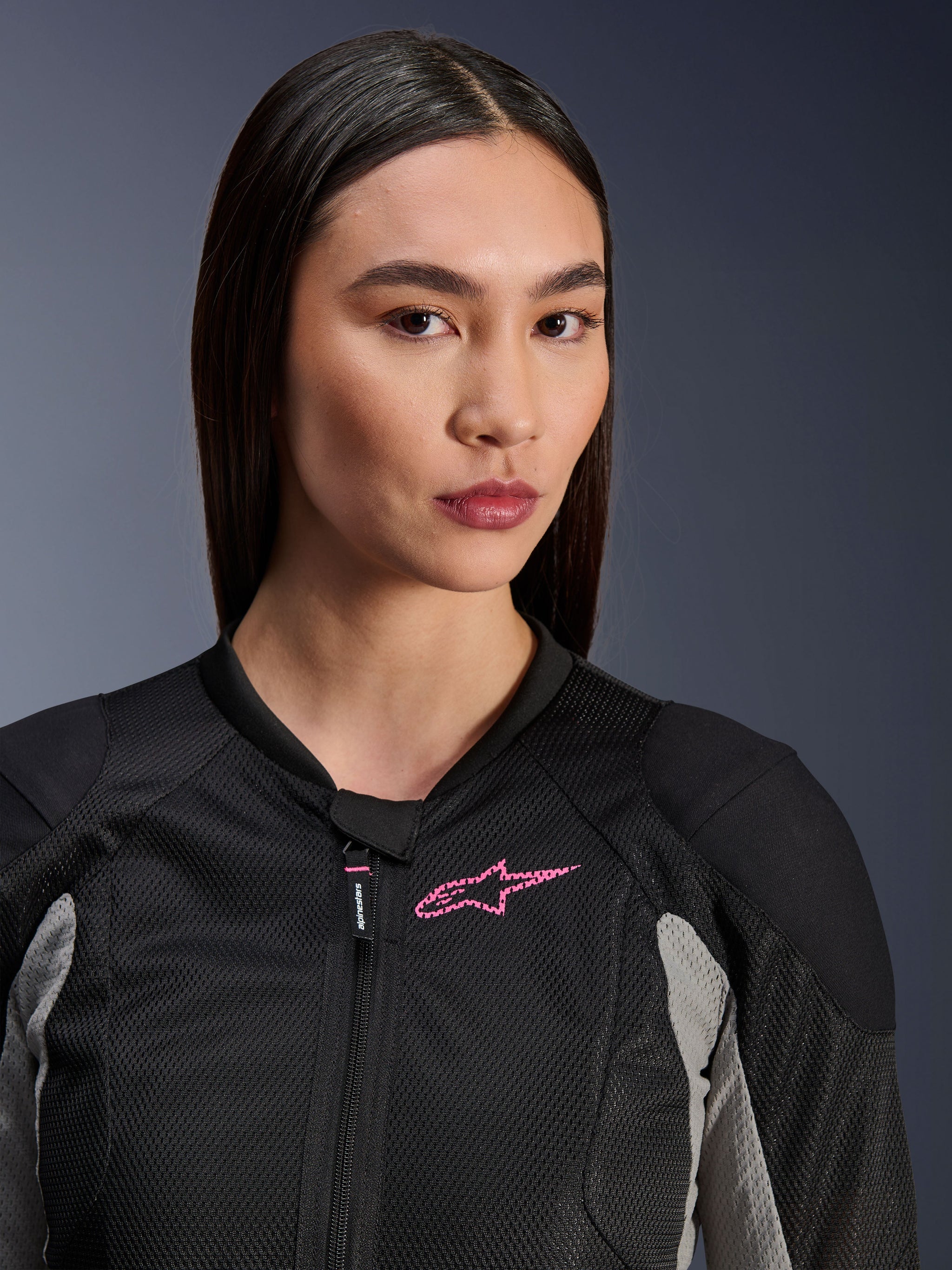 Woman wearing the Alpinestars Stella Troop-Air Jacket, Black Ash Gray and Pink Fluo, close-up view highlighting the technical mesh construction and pink chest logo, stylish urban motorcycle gear