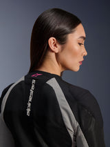 Close-up profile of a woman wearing the Alpinestars Stella Troop-Air Jacket, Black and Ash Gray mesh construction, vertical white Alpinestars logo on the upper back with a Pink Fluo star logo, lightweight technical motorcycle gear for women