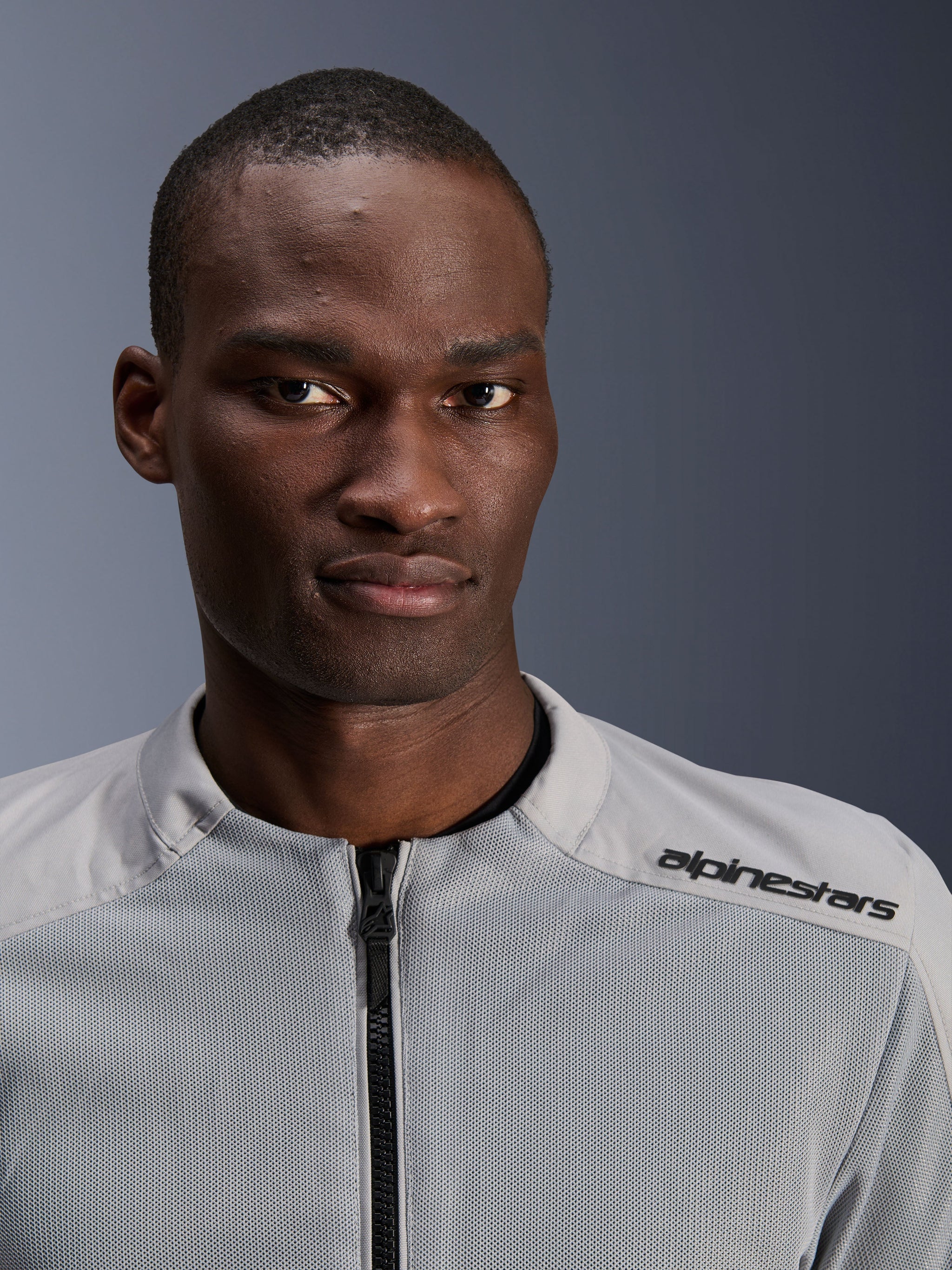 Alpinestars C-1 Air Jacket in Silver and Gray, close-up portrait of a male rider, featuring technical mesh panels and black branding on the shoulder, urban contemporary motorcycle gear