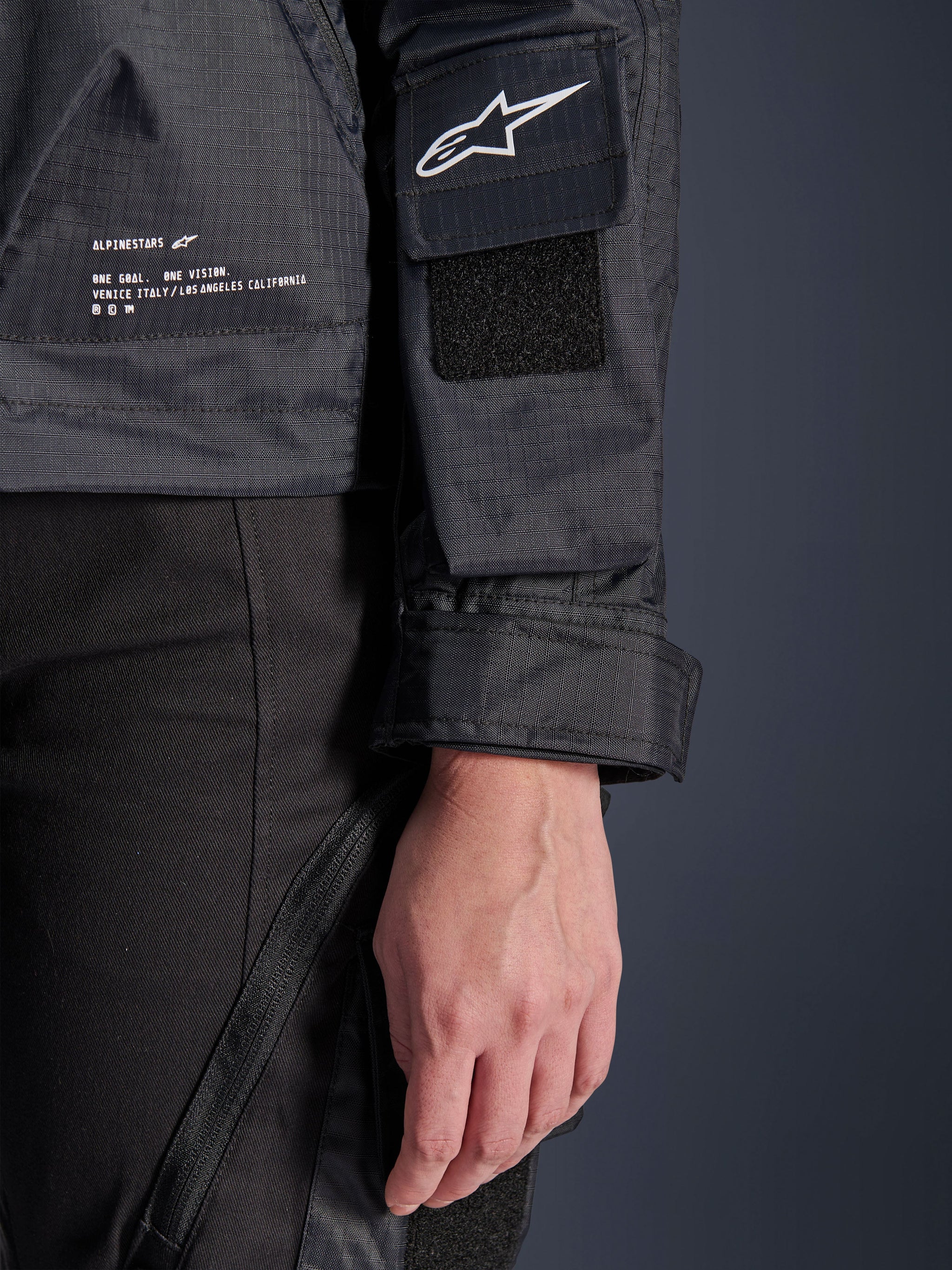 Alpinestars Molly Air Jacket, close-up detail of black ripstop textile, white Astar logo on sleeve pocket with velcro patch, adjustable cuff, and printed branding text on the side, urban motorcycle gear for women