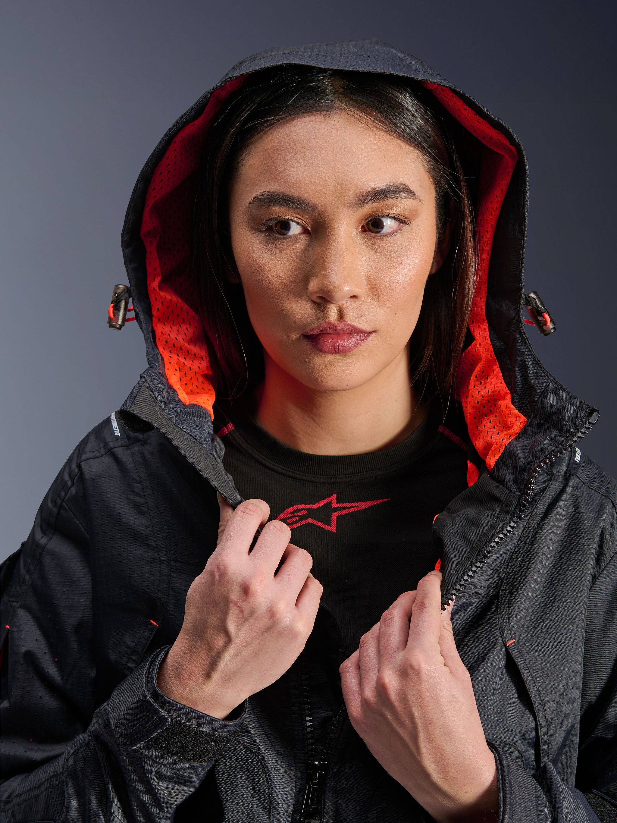 Alpinestars Molly Air Jacket, Women's Motorcycle Jacket, Black and Fluo Coral, model wearing the hood up showing vibrant coral mesh lining, ripstop textile fabric, urban contemporary riding gear