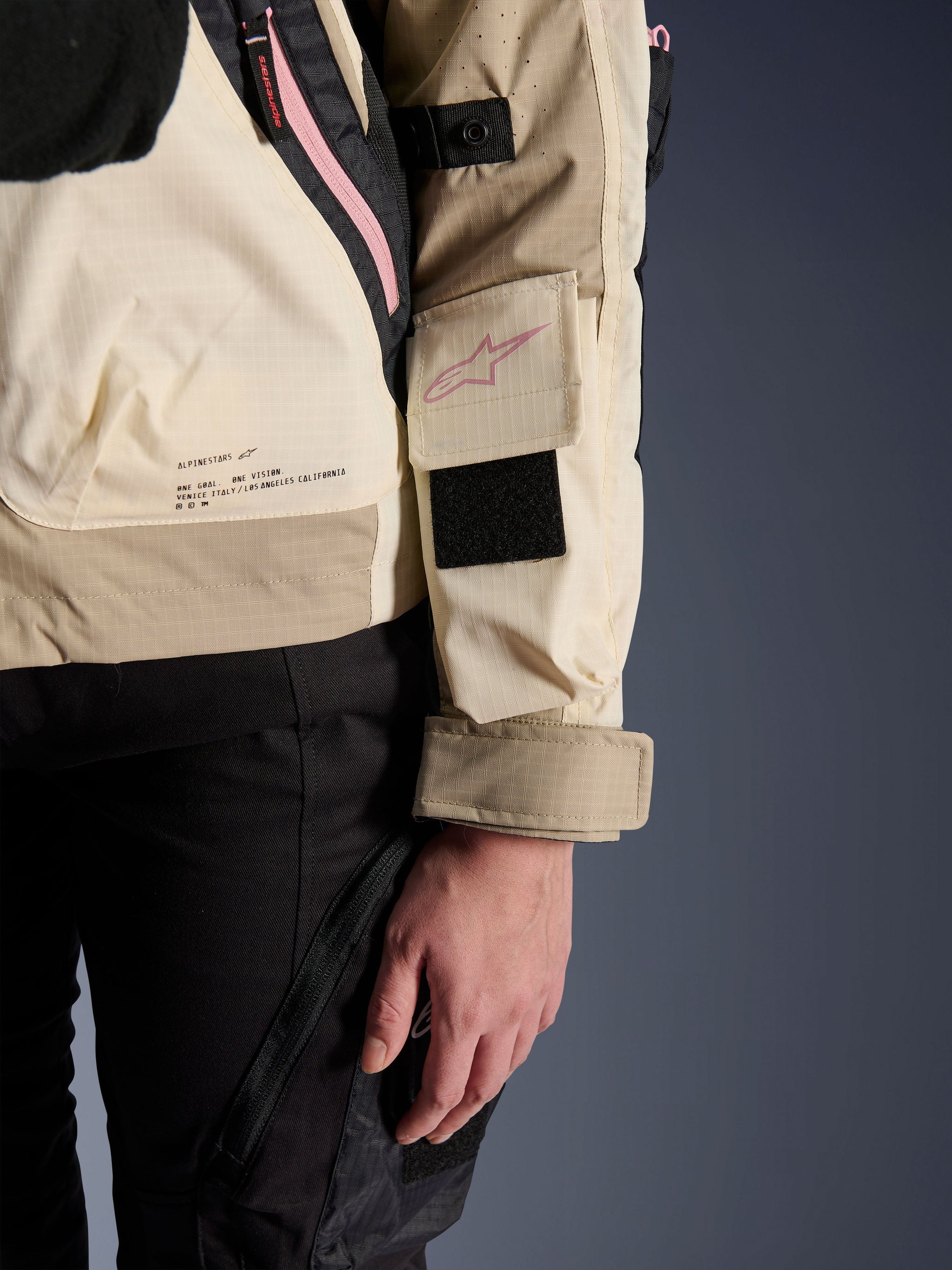 Alpinestars Molly Air Jacket, Women's Urban Motorcycle Jacket, Sand Pink Almond, close-up side view showing sleeve pocket with pink logo, black Velcro patch, and brand mission text on lower back, lightweight ripstop material