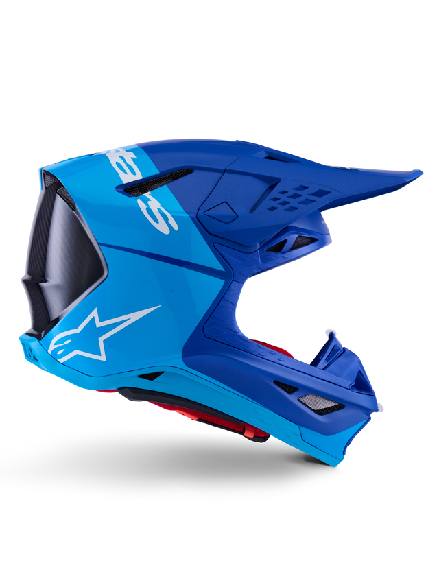 Alpinestars Supertech M10 Flood Helmet, Motocross Helmet, Metallic and Medium Blue with Black Carbon accents, side profile view, featuring a white logo, aerodynamic design with ventilation ports, carbon fiber texture details, professional off-road racing protection