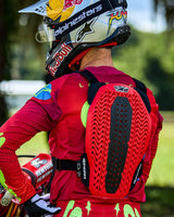 Motocross rider seen from behind wearing the Alpinestars A-5 Plasma Chest Protector, featuring a red and black back protector with a ventilated honeycomb structure, worn over a red long-sleeve jersey with a Red Bull branded helmet.