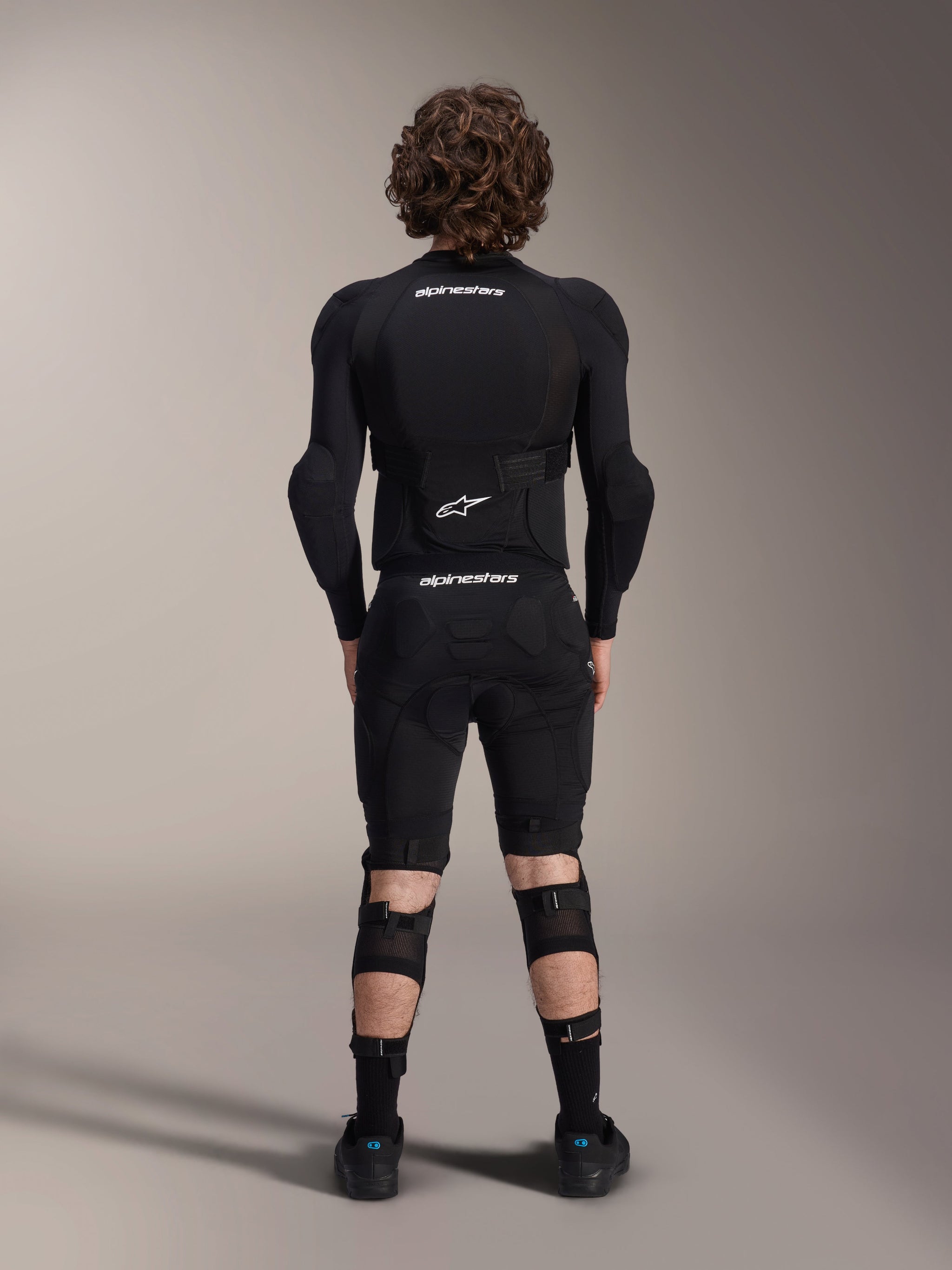 Alpinestars A-Impact Plasma Protection Jacket - Long Sleeve, back view, black with white Alpinestars logos, worn with protective shorts and knee guards for full-body mountain bike protection
