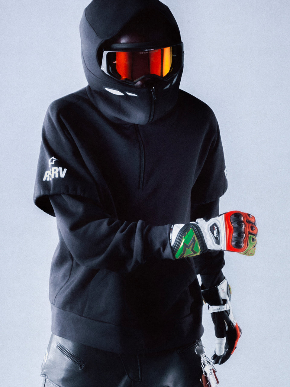 RSRV Vault Hoodie, Black Premium Streetwear Hoodie, Person wearing motorsport-inspired luxury hoodie with hood up, black helmet with reflective red-orange goggles, colorful racing gloves, sleek urban performance style