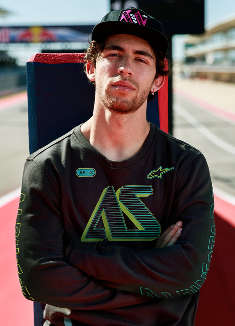 Alpinestars Ayess Csf Tee, Long Sleeve T-Shirt, Black, featuring green and yellow gradient AS graphics on the chest and sleeves, casual motorsport-inspired streetwear worn at a racetrack