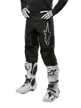 Alpinestars 2024 Fluid Graphite Pants, Motocross Pants, Black and Silver, featuring a silver Alpinestars logo on the thigh, shown worn with white motocross boots and gloves, designed for off-road motorcycle racing