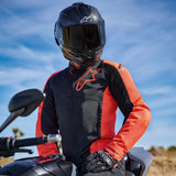 Alpinestars Viper Air V4 Jacket in Red Fluo and Black, worn by a rider on a motorcycle, featuring a large chest logo and ventilated mesh panels, paired with a carbon fiber helmet and black gloves, road and sport motorcycling gear