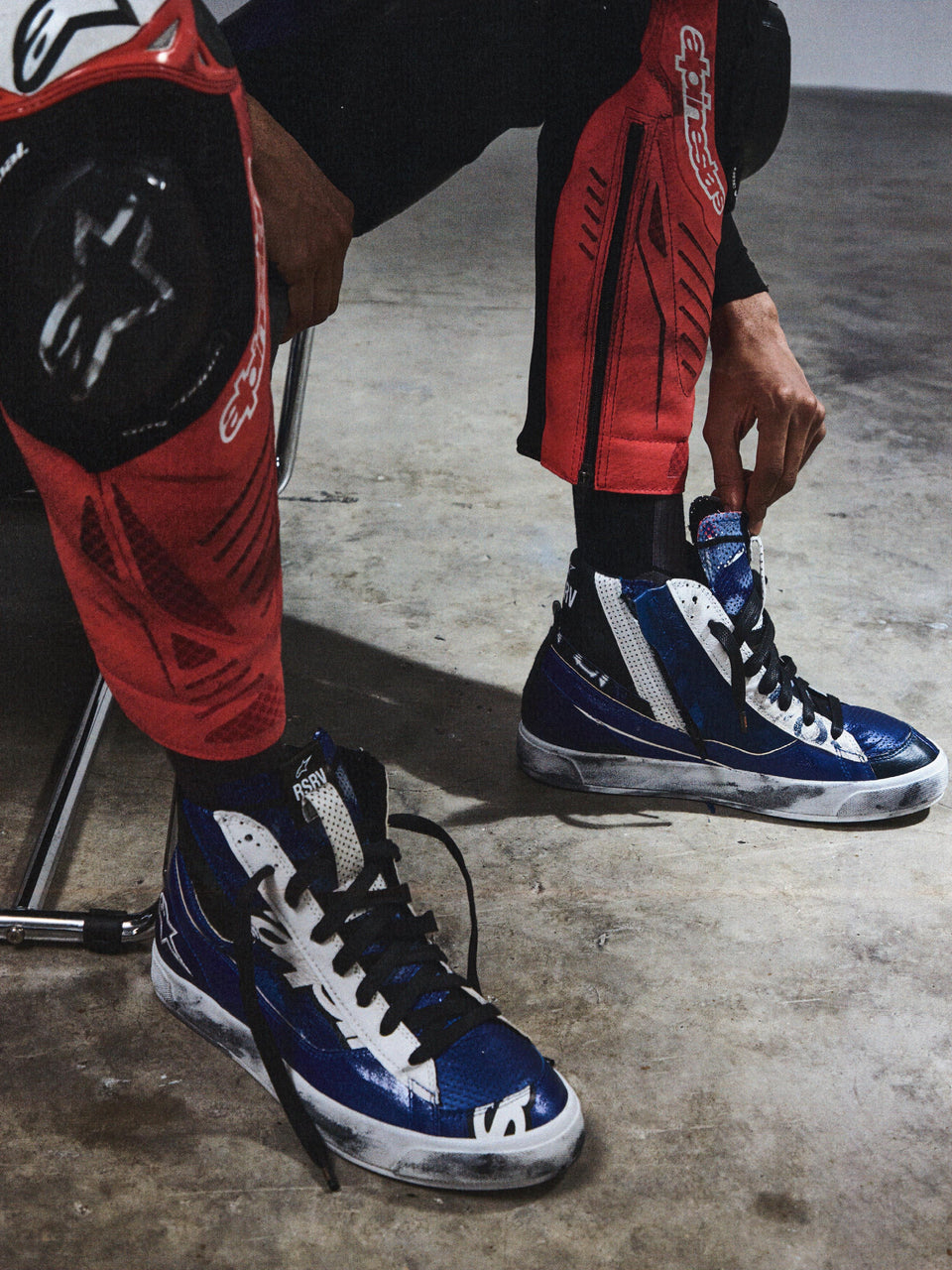 Alpinestars RSRV Legacy Shoe, High-Top Sneakers, Blue and White, Worn with Red and Black Protective Pants, Urban Motorcycle Footwear, Black Laces, Lifestyle Motorsport Style