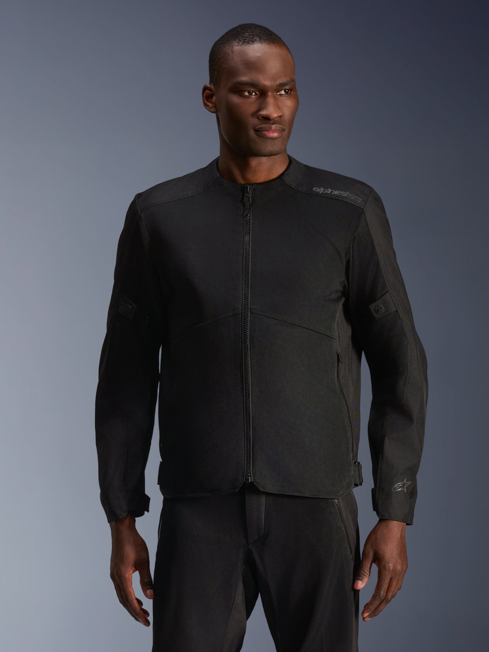 Male model wearing Alpinestars C-1 Air Jacket in Black, contemporary motorcycle jacket with extensive tech mesh panels and a full front zipper, paired with matching black riding pants, urban lifestyle and commuting aesthetic